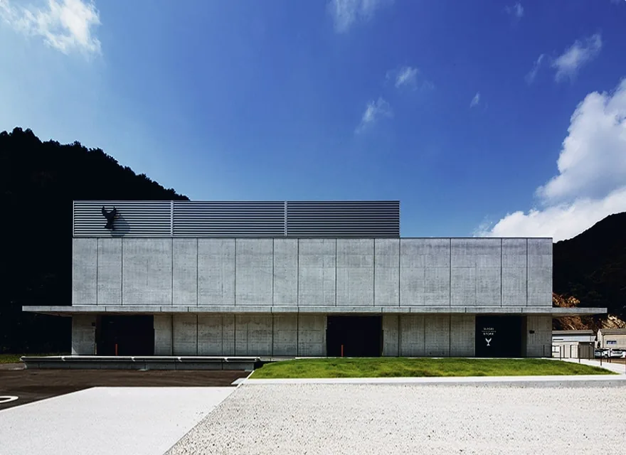 醉鯨酒造土佐藏:方正的清水模建築,屋頂掛著鯨魚標誌,背後是山和藍天